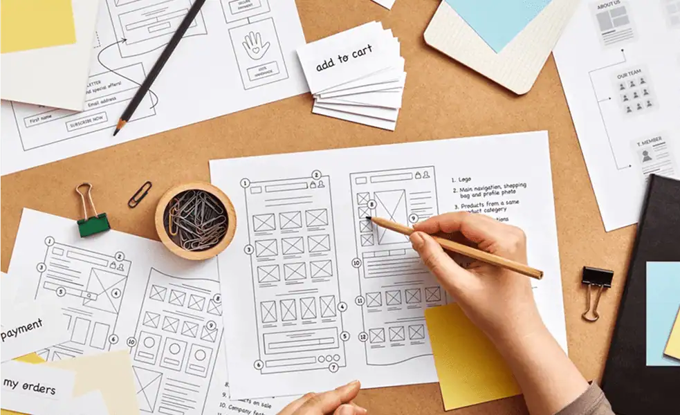Workspace with sketches and drafts of logo designs on paper, featuring geometric shapes and letter-based concepts.